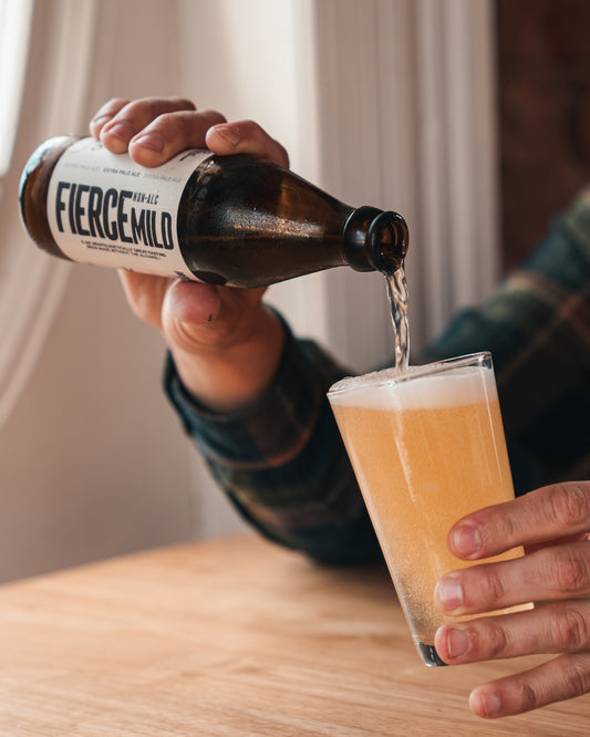 Non alcoholic beer from a brown glass bottle of Fierce Mild pours into a drinking glass from a height