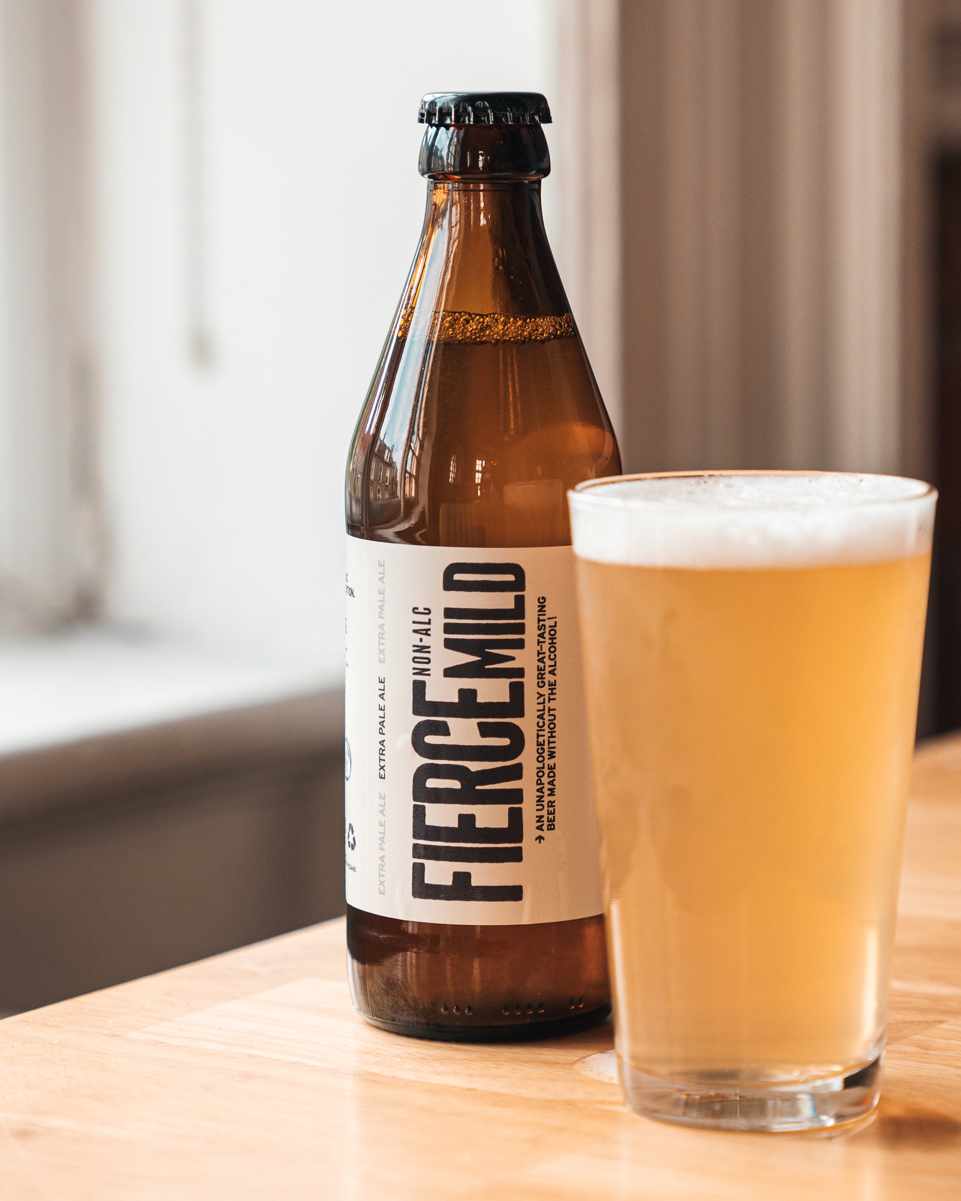 Unopened brown glass bottle of Fierce Mild non-alc beer sits next to glass filled with beer.