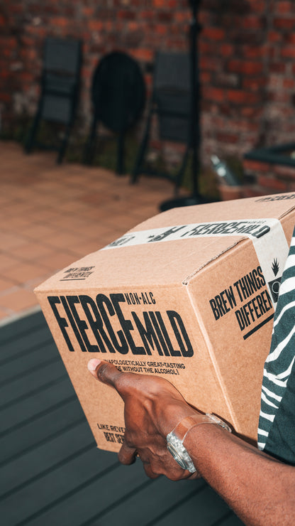 Arm with wrist watch is shown holding Fierce Mild non-alc beer packaged in a branded craft brown box with white branded label tape.